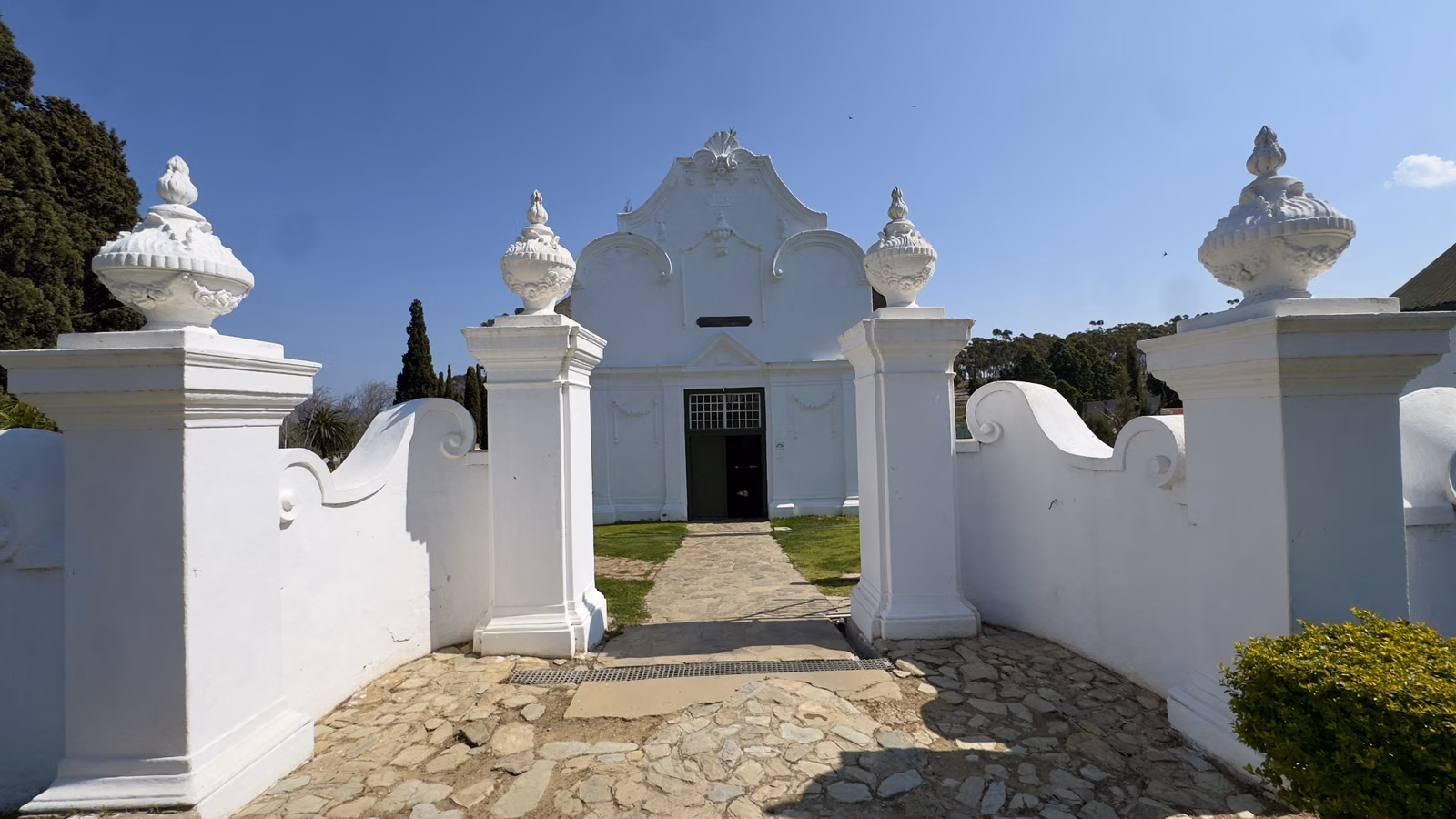 De Oude Kerk — the whitewashed gabled church seen through its urn-topped entrance wall